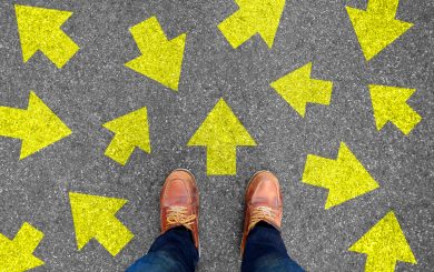 Feet and arrows on road background. Taking decisions for the future with many arrows choices, left right or move forward. Hipster in boots or brown shoes standing on pathway. Top view.