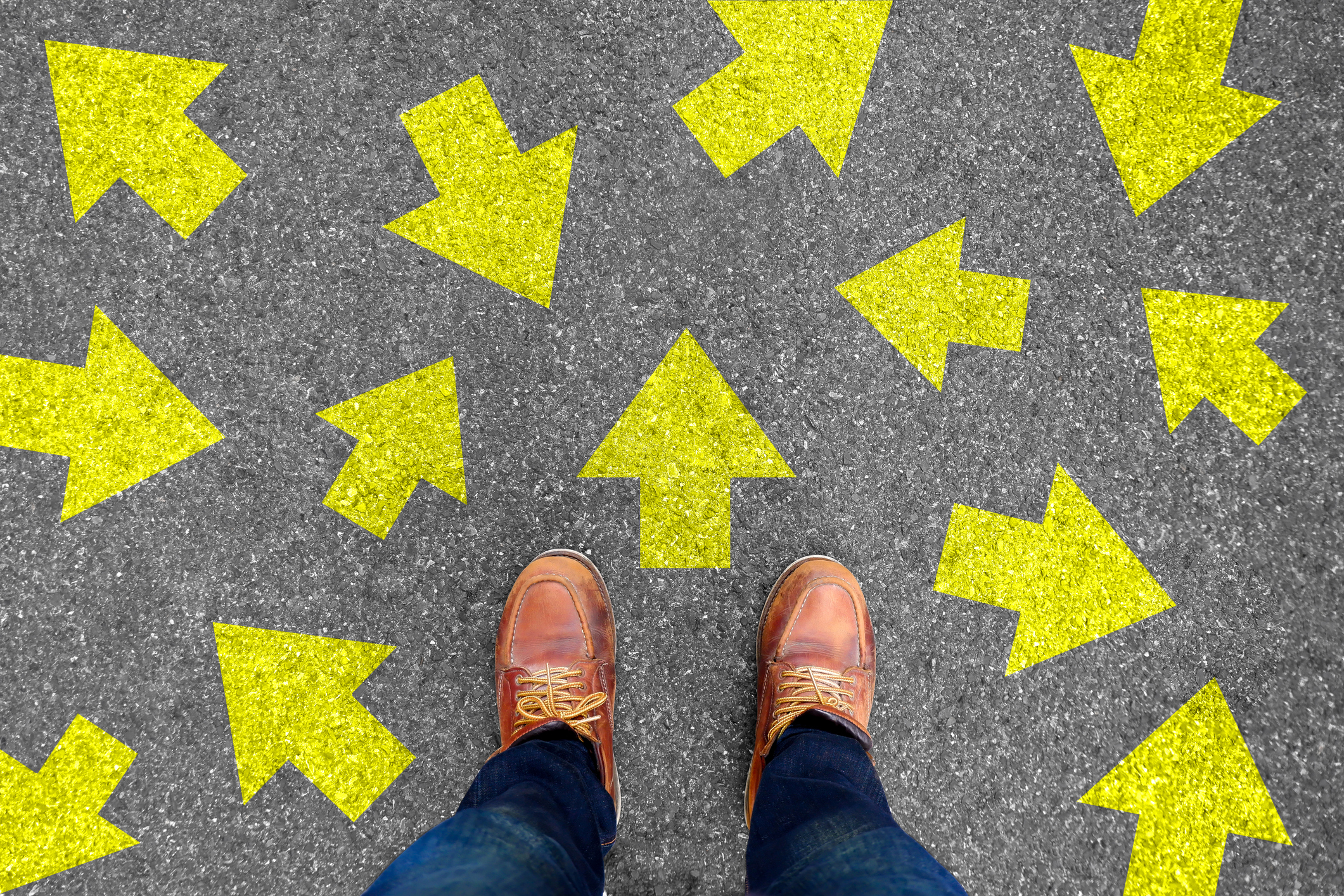 Feet and arrows on road background. Taking decisions for the future with many arrows choices, left right or move forward. Hipster in boots or brown shoes standing on pathway. Top view.